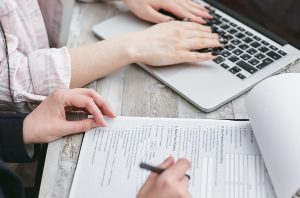 Hands close-up, filling out loan application on paper and a laptop computer for article about a Comparison of Loan Types